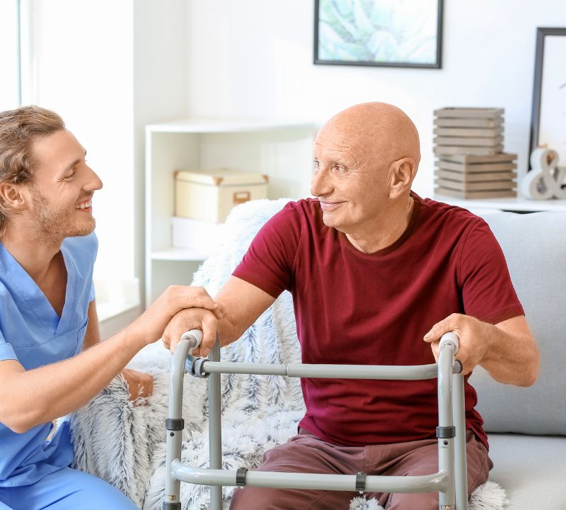 A caretaker helping an elderly man stand up from a chair